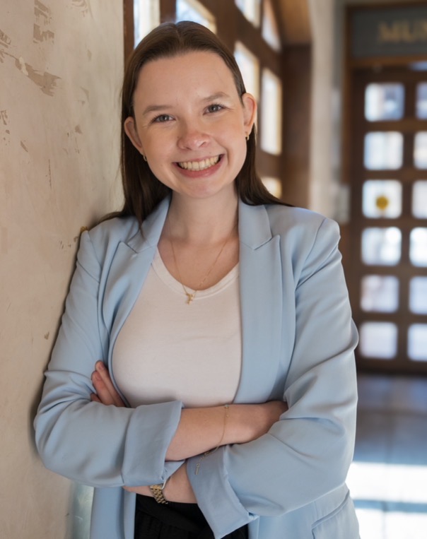 Katie is standing in front of doors with sunlight coming through